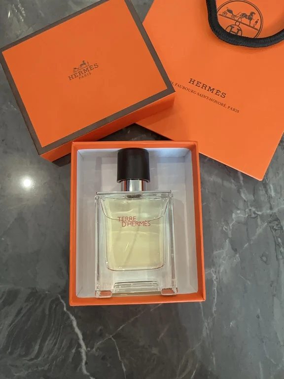 زجاجة عطر تير ديرميس موضوعة في علبة هدايا برتقالية مفتوحة بجانب حقيبة تسوق هيرميس