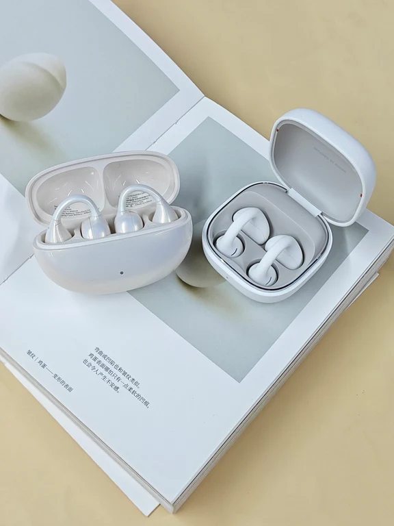 Two different open earphone charging cases displaying white and silver clip earbuds on an open book.