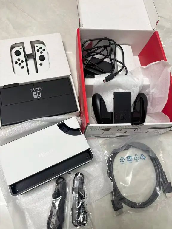 Unboxing view of the Nintendo Switch OLED showing the wide kickstand on the console, white dock, and accessories