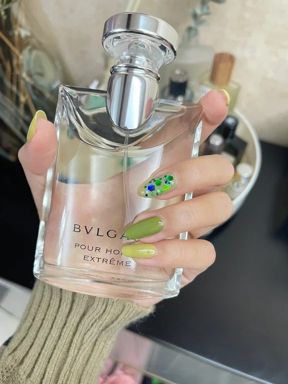 A hand holding a clear bottle of Bvlgari Pour Homme Extreme perfume.