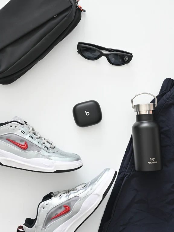 Workout gear flat lay featuring sneakers, sunglasses, water bottle, and a black Beats charging case