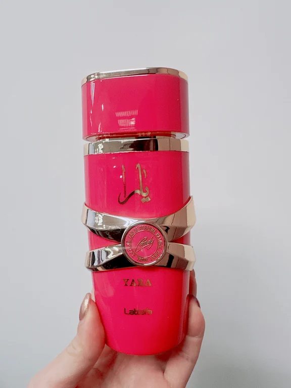 Hand holding a vibrant hot pink Lattafa Yara Candy Eau de Parfum bottle with gold metallic bands.
