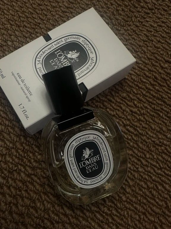 Diptyque L'Ombre Dans L'Eau perfume bottle resting on top of its white cardboard retail box