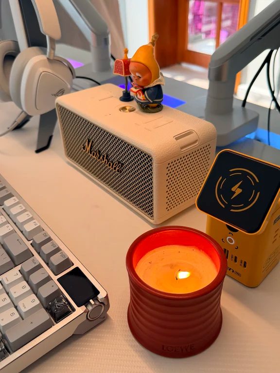 Off-white compact Marshall portable speaker on a computer desk next to a burning candle and mechanical keyboard