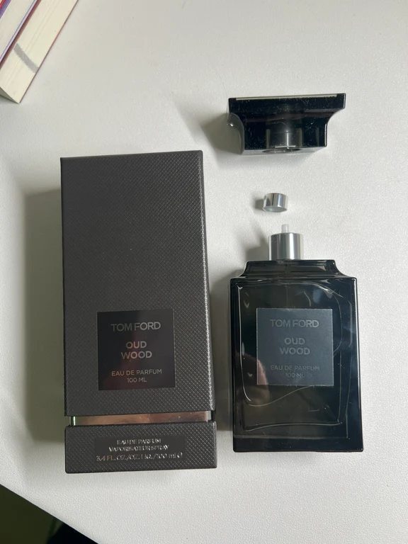 زجاجة عطر توم فورد عود وود 100 مل بدون غطاء بجوار علبة التغليف الرمادية