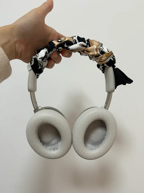Hand holding cream over-ear headphones with a patterned silk ribbon wrapped decoratively along the headband cushion.
