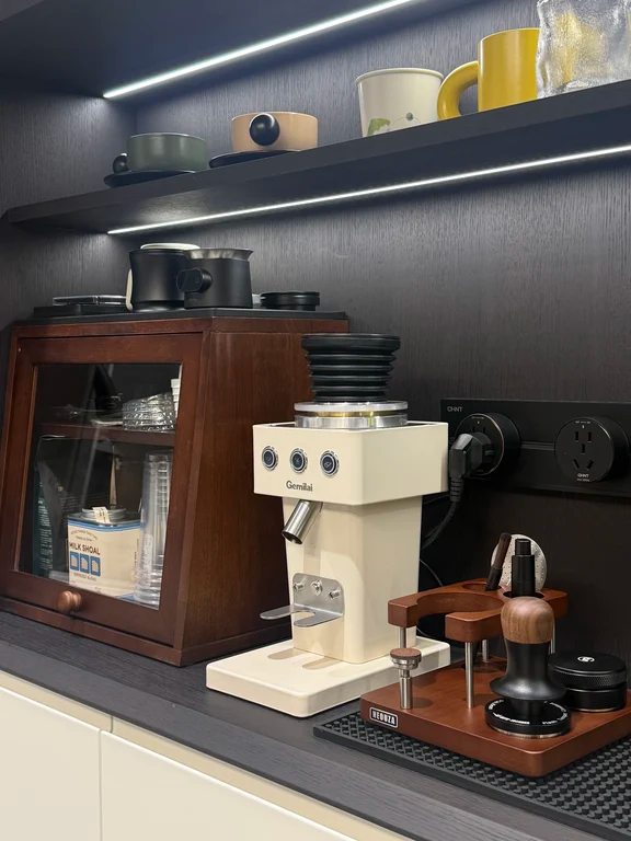 Cream-colored Gemilai burr coffee grinder with tamping station accessories on a shelf