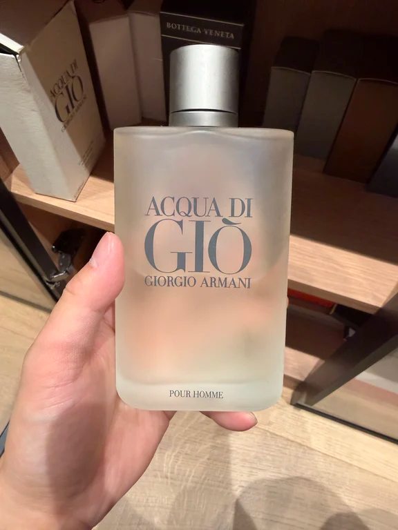 A hand holding a frosted glass bottle of Giorgio Armani Acqua Di Giò Pour Homme fragrance.