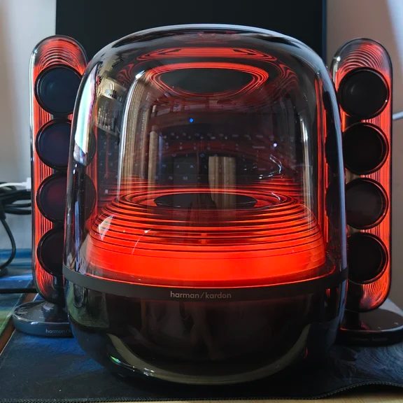 Harman Kardon SoundSticks system featuring a clear dome subwoofer glowing orange-red flanked by transparent satellite speakers