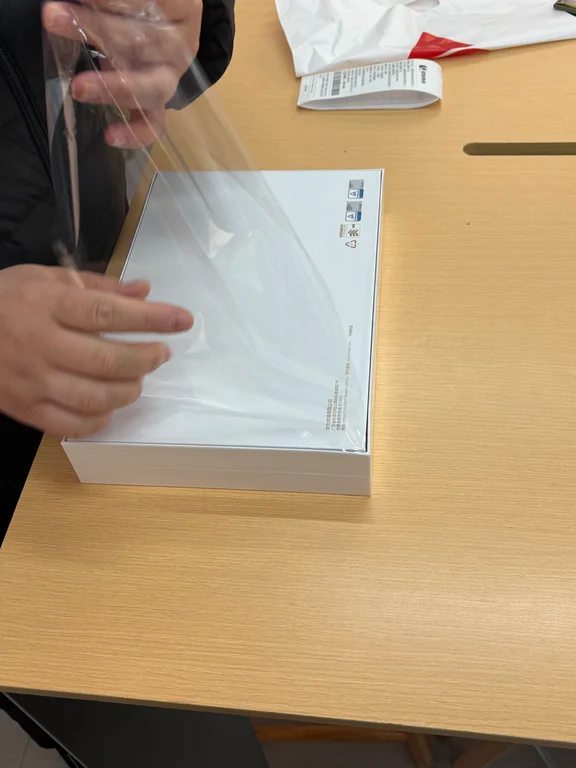 Hands peeling clear protective plastic film from a tablet packaging box.
