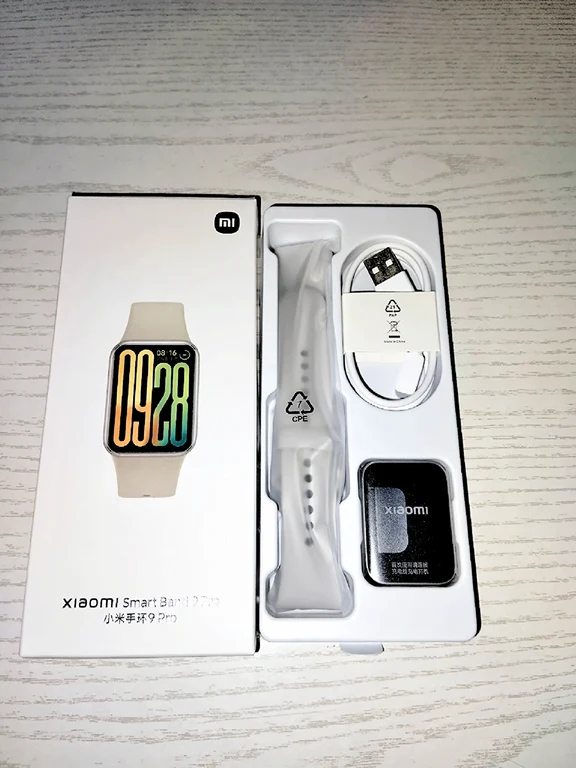 Unboxed Xiaomi Smart Band 9 Pro showing the rectangular watch unit, white silicone strap, and charging cable in plastic tray